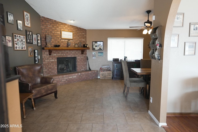 living room with ceiling fan, lofted ceiling, a fireplace, and light tile patterned floors