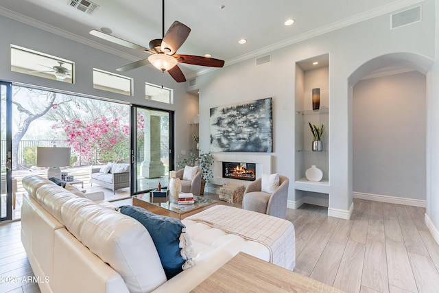 living area featuring a glass covered fireplace, wood finished floors, visible vents, and crown molding