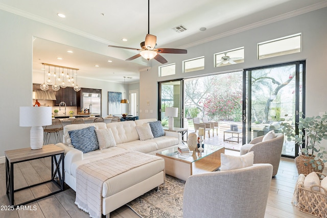 living room with recessed lighting, a ceiling fan, visible vents, ornamental molding, and light wood finished floors