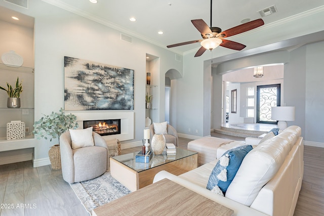 living room with wood finished floors, a glass covered fireplace, visible vents, and crown molding