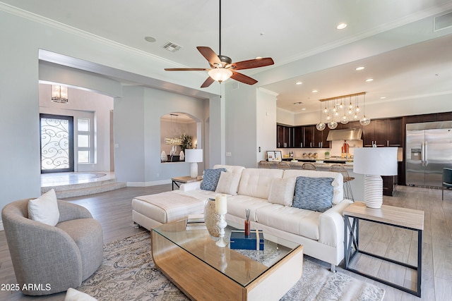 living room featuring ornamental molding, light wood-style flooring, visible vents, and baseboards