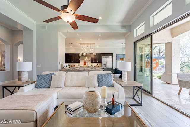 living area with arched walkways, recessed lighting, ceiling fan with notable chandelier, visible vents, and ornamental molding