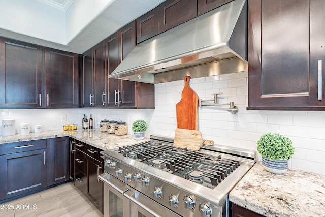 kitchen featuring tasteful backsplash, light stone counters, stainless steel gas range, crown molding, and under cabinet range hood