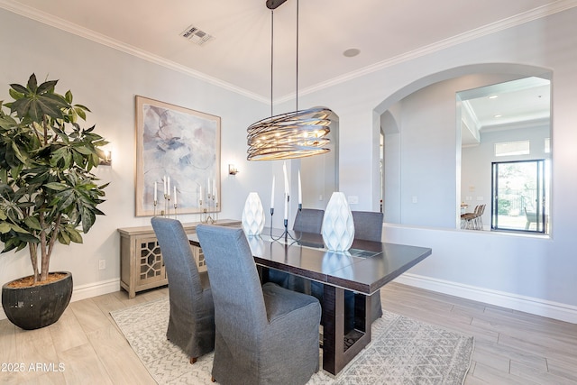 dining space featuring arched walkways, crown molding, visible vents, light wood-type flooring, and baseboards