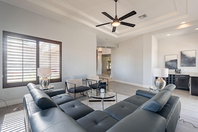 living room with ceiling fan, a tray ceiling, visible vents, and baseboards