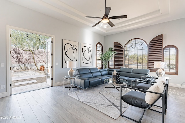 living area featuring a tray ceiling, wood finished floors, and baseboards