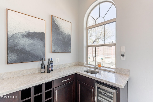 kitchen featuring light stone counters, wine cooler, a sink, and dark brown cabinetry