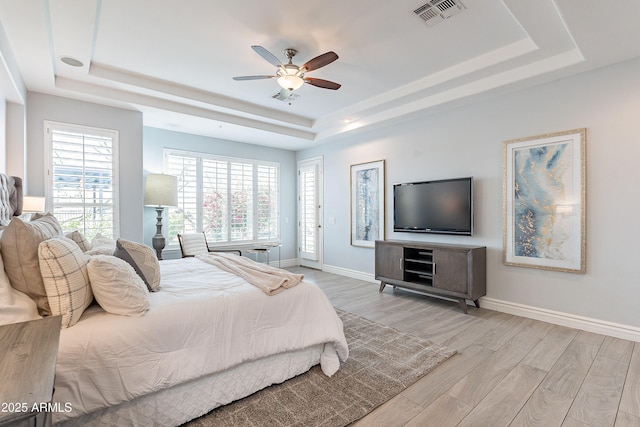 bedroom featuring a raised ceiling, visible vents, light wood-style flooring, and baseboards