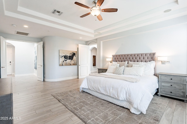 bedroom featuring visible vents, arched walkways, a tray ceiling, and wood finished floors