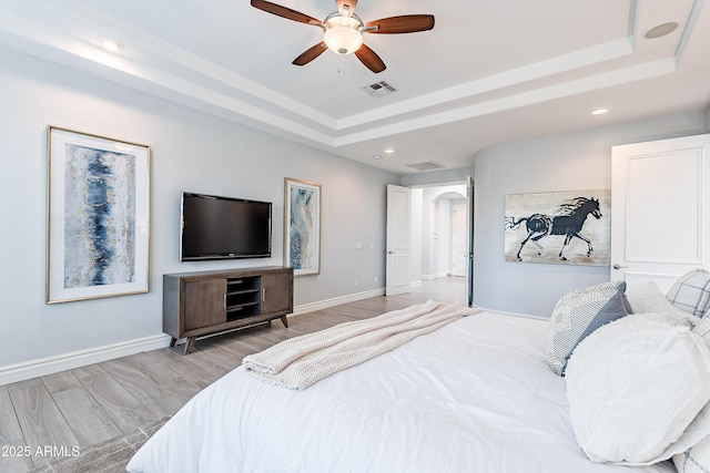 bedroom featuring visible vents, a raised ceiling, arched walkways, and wood finished floors