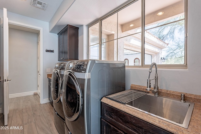 clothes washing area featuring separate washer and dryer, a sink, visible vents, light wood-style floors, and cabinet space