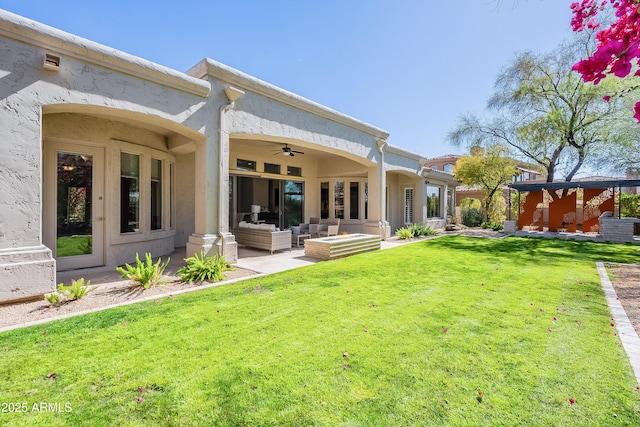 rear view of property featuring ceiling fan, outdoor lounge area, a lawn, stucco siding, and a patio area