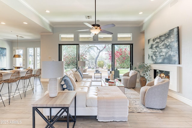 living room featuring light wood finished floors, visible vents, a glass covered fireplace, crown molding, and recessed lighting