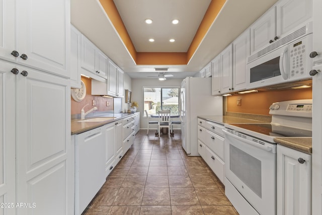 kitchen featuring sink, white appliances, tile patterned flooring, a tray ceiling, and white cabinets