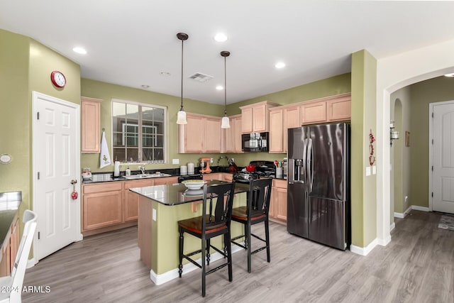 kitchen featuring decorative light fixtures, a breakfast bar, a kitchen island, black appliances, and light wood-type flooring