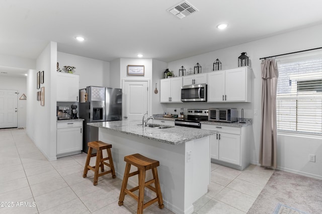 16617 W Desert Mirage Dr, Surprise, AZ 85388 - kitchen featuring appliances with stainless steel finishes, a sink, light tile patterned floors, light stone counters, and a kitchen breakfast bar