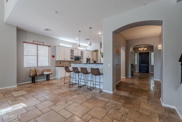2735 E Flower Ct, Gilbert, AZ 85298 - kitchen with arched walkways, stone tile flooring, a breakfast bar, white cabinetry, and stainless steel microwave
