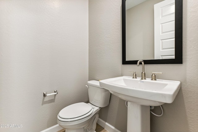 bathroom with a sink, baseboards, toilet, and a textured wall