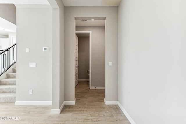 corridor featuring stairway, visible vents, baseboards, and wood finish floors