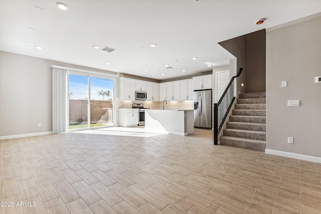 unfurnished living room featuring light wood finished floors, visible vents, baseboards, stairs, and a sink