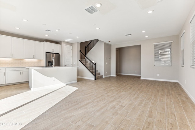 kitchen featuring visible vents, stainless steel refrigerator with ice dispenser, tasteful backsplash, white cabinetry, and light wood-style floors