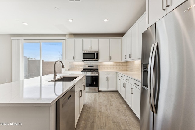 kitchen featuring a sink, decorative backsplash, appliances with stainless steel finishes, and a center island with sink