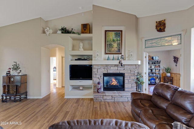 living room featuring high vaulted ceiling, light hardwood / wood-style floors, and a stone fireplace