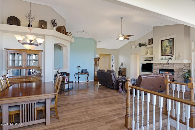 dining room with a stone fireplace, built in features, vaulted ceiling, ceiling fan with notable chandelier, and hardwood / wood-style flooring