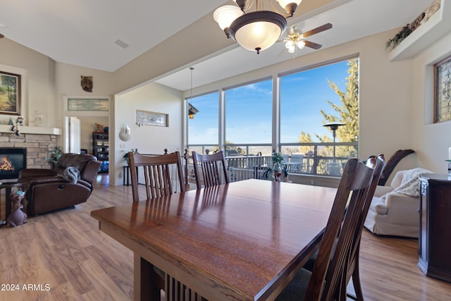 dining space with light wood-type flooring, a stone fireplace, ceiling fan, and vaulted ceiling