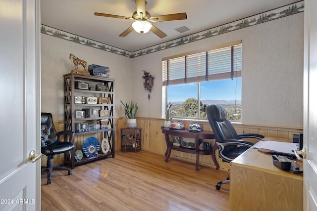 home office featuring light wood-type flooring, ceiling fan, and wood walls