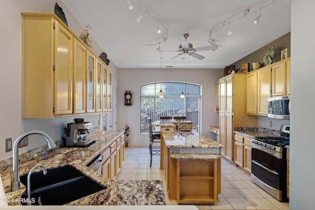 kitchen with light stone countertops, ceiling fan, sink, stainless steel appliances, and a center island with sink