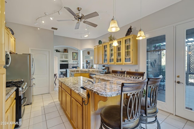 kitchen with hanging light fixtures, light tile patterned floors, light stone countertops, a kitchen bar, and stainless steel appliances