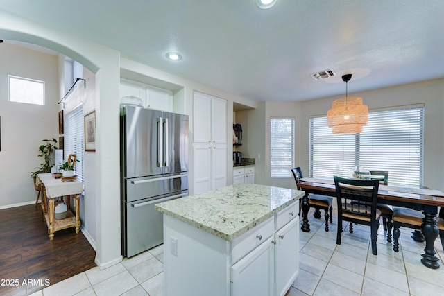 kitchen with light stone counters, light tile patterned floors, visible vents, freestanding refrigerator, and white cabinetry