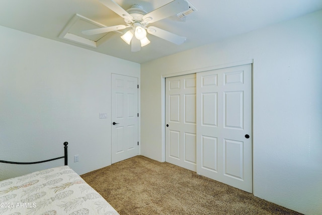 unfurnished bedroom with attic access, a closet, ceiling fan, and carpet flooring