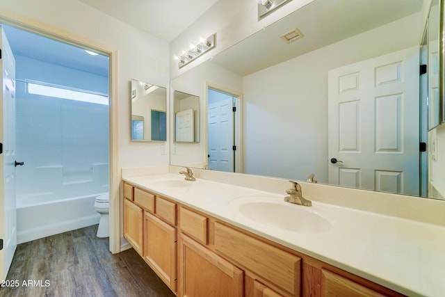 full bathroom with toilet, double vanity, a sink, and wood finished floors