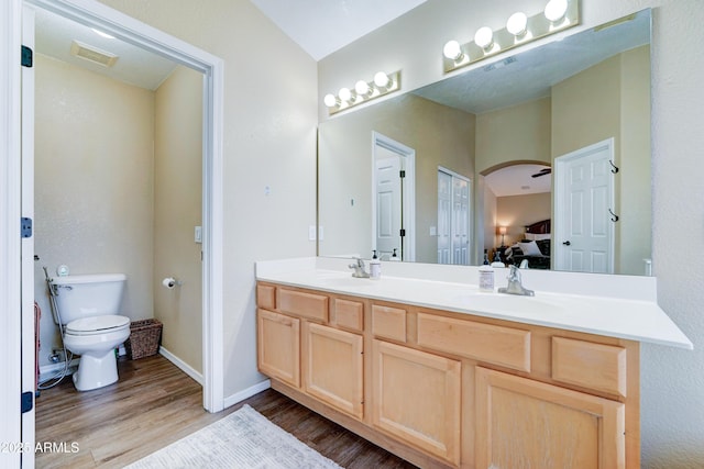 ensuite bathroom with visible vents, connected bathroom, toilet, wood finished floors, and a sink