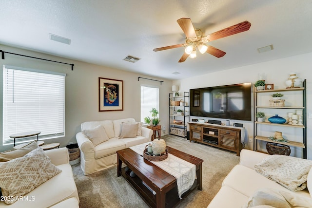 living area with ceiling fan, visible vents, and light colored carpet