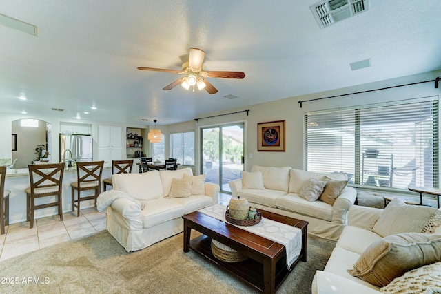 living room with a ceiling fan, arched walkways, visible vents, and light tile patterned floors