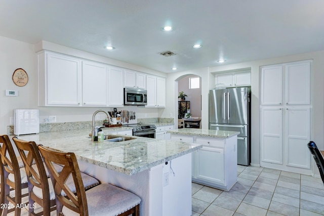 kitchen featuring arched walkways, stainless steel appliances, a peninsula, a sink, and visible vents