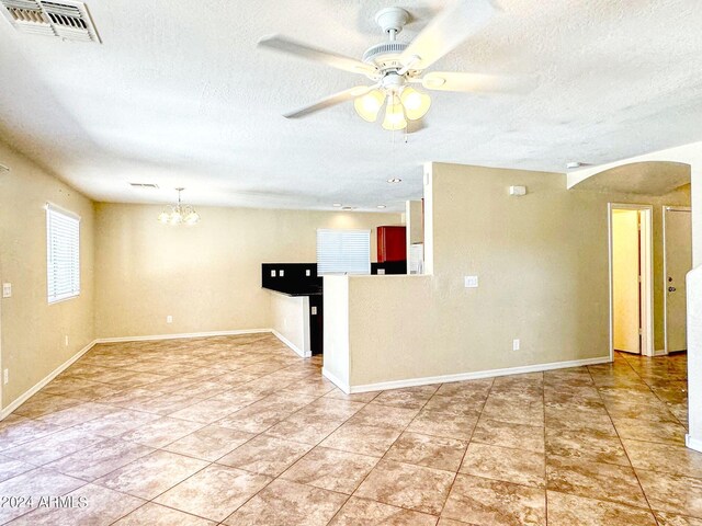 tiled empty room featuring ceiling fan with notable chandelier