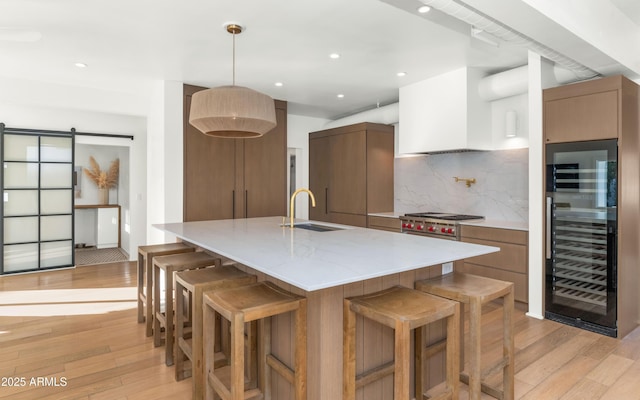 kitchen featuring a barn door, beverage cooler, light wood finished floors, and a sink