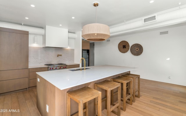 kitchen with a breakfast bar area, light wood-style floors, visible vents, and a sink