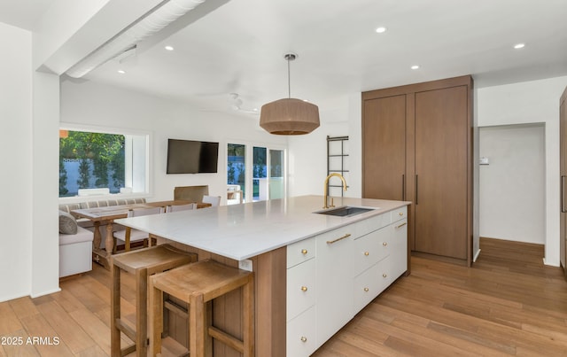 kitchen with open floor plan, a center island with sink, light wood-style floors, and a sink