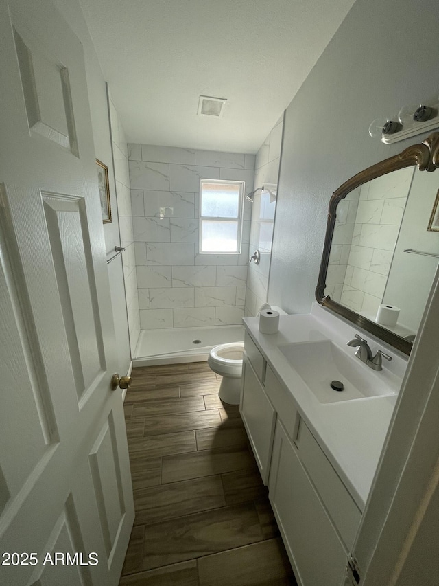 bathroom with tiled shower, vanity, and toilet