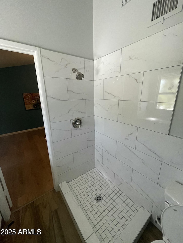 bathroom with wood-type flooring, tiled shower, and toilet