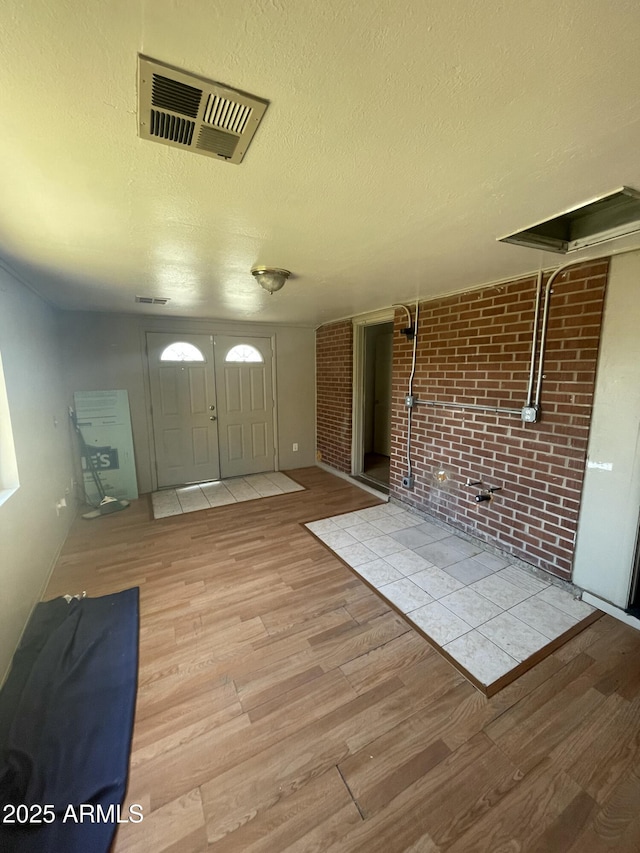 entryway with brick wall, a textured ceiling, and light hardwood / wood-style flooring