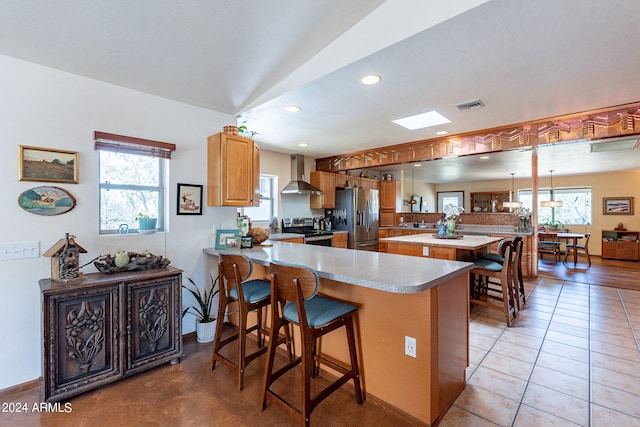 kitchen with stainless steel appliances, a kitchen bar, wall chimney exhaust hood, and a healthy amount of sunlight