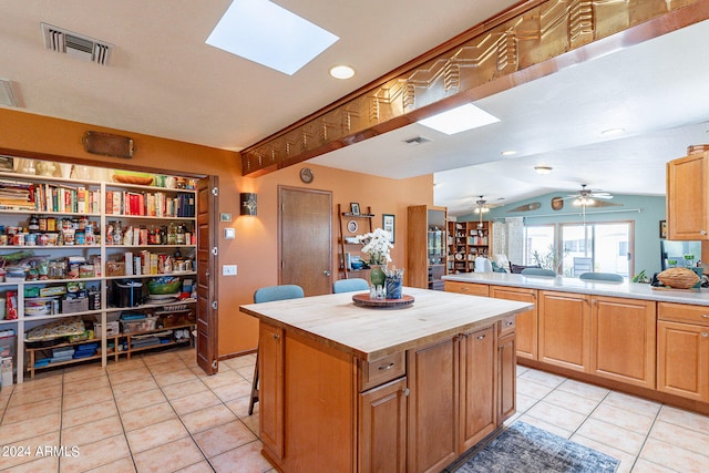 kitchen featuring light tile floors, a center island, vaulted ceiling with skylight, and ceiling fan