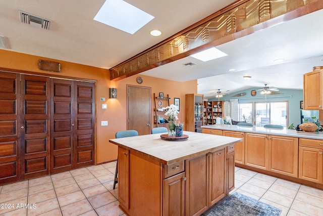 kitchen with vaulted ceiling with skylight, ceiling fan, a kitchen island, and light tile flooring