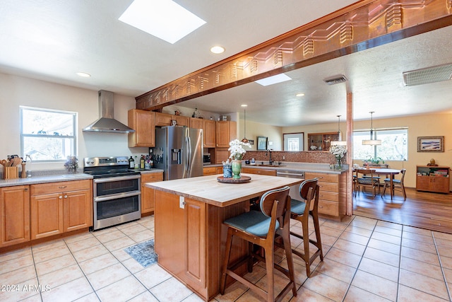 kitchen featuring appliances with stainless steel finishes, a center island, a healthy amount of sunlight, and wall chimney range hood